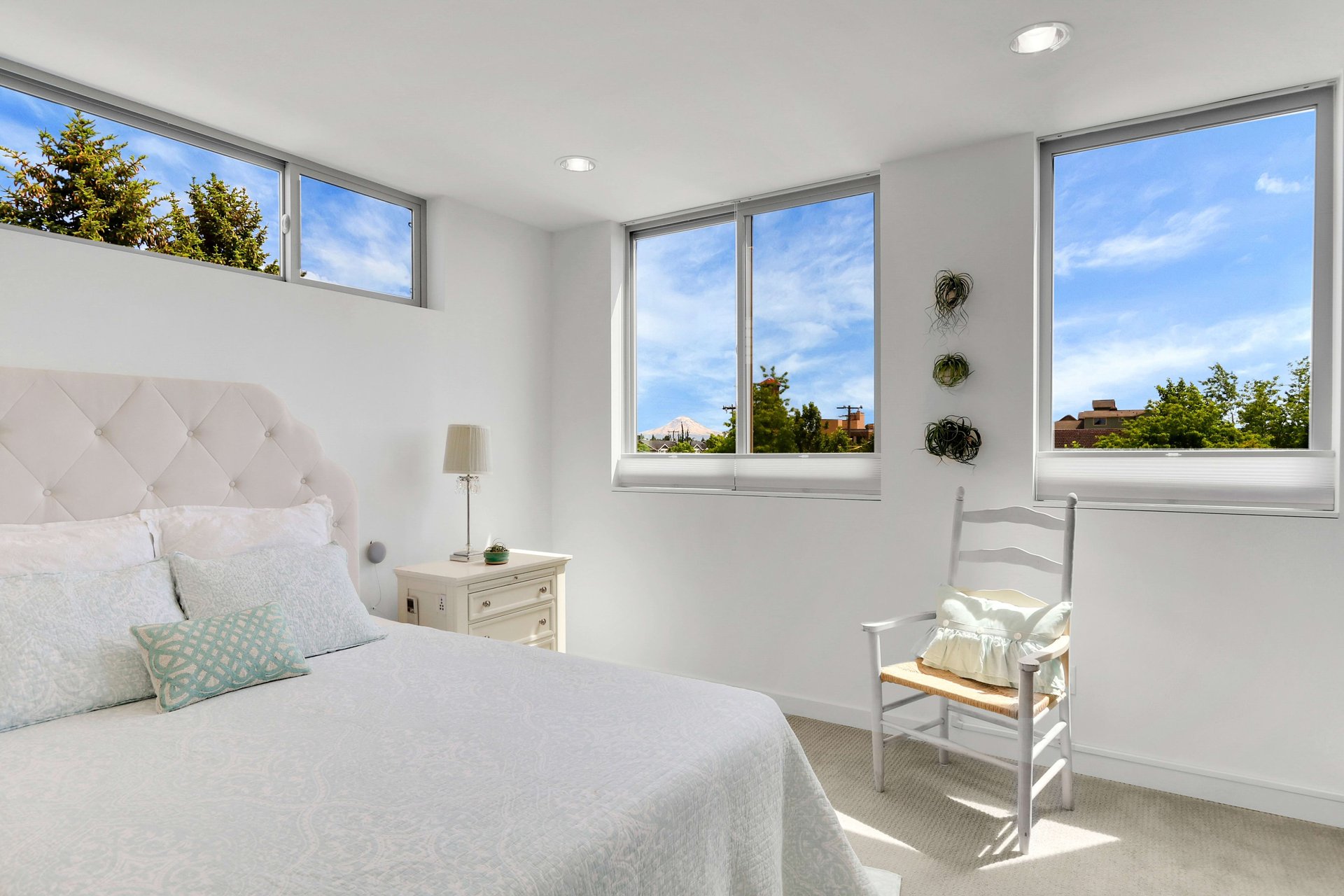 Bright bedroom with a tufted white bed, wide windows, and a distant mountain view.