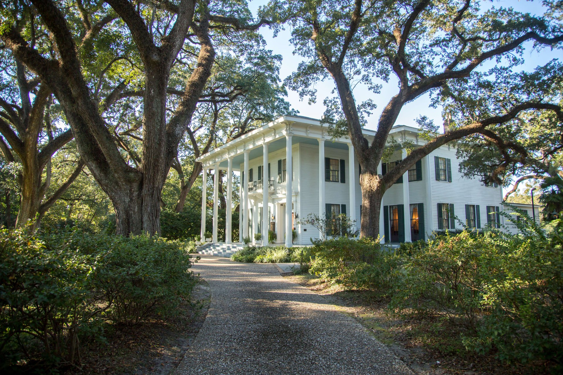 A white mansion with black shutters, surrounded by trees.