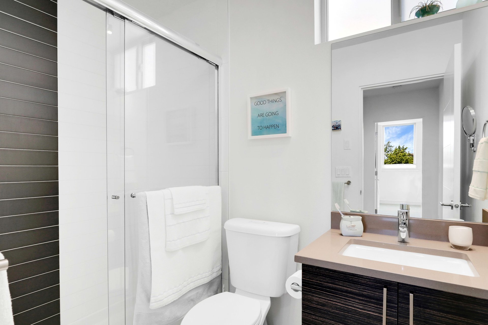 Bright bathroom with glass-enclosed shower, dark tile, and dark wood vanity.