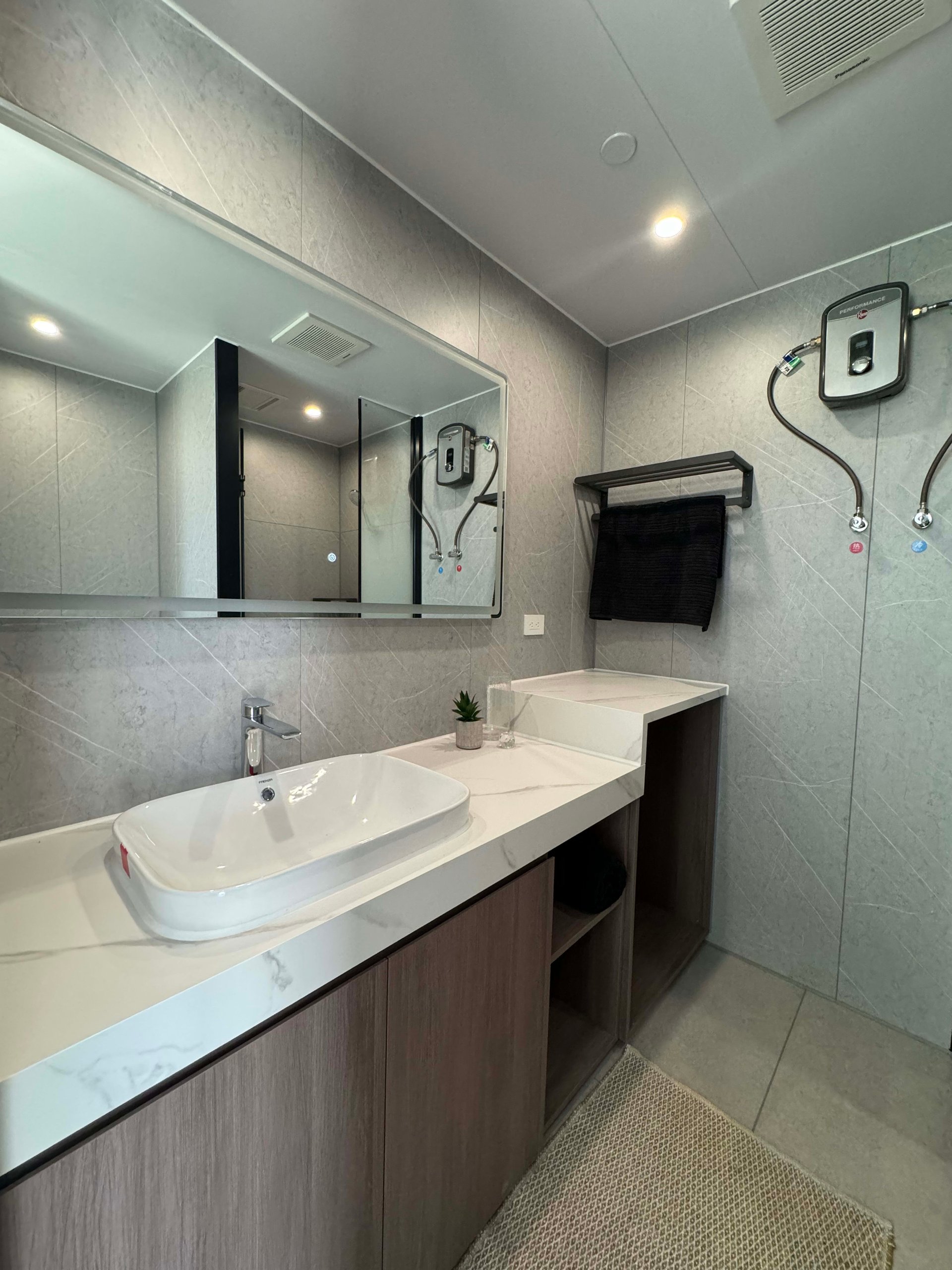 Modern bathroom with a white vessel sink, marble-look vanity counter, and gray tiled walls.