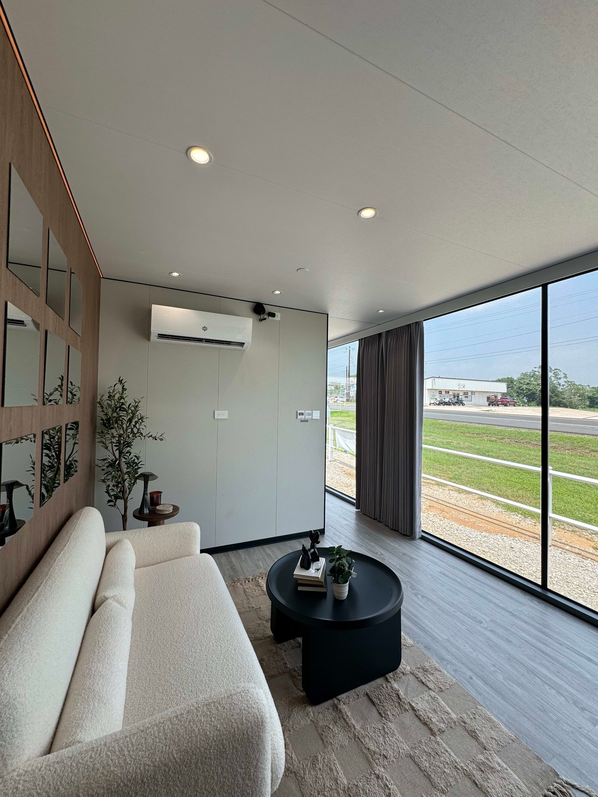Tiny home living room with a cream sofa, black coffee table, and floor-to-ceiling windows.