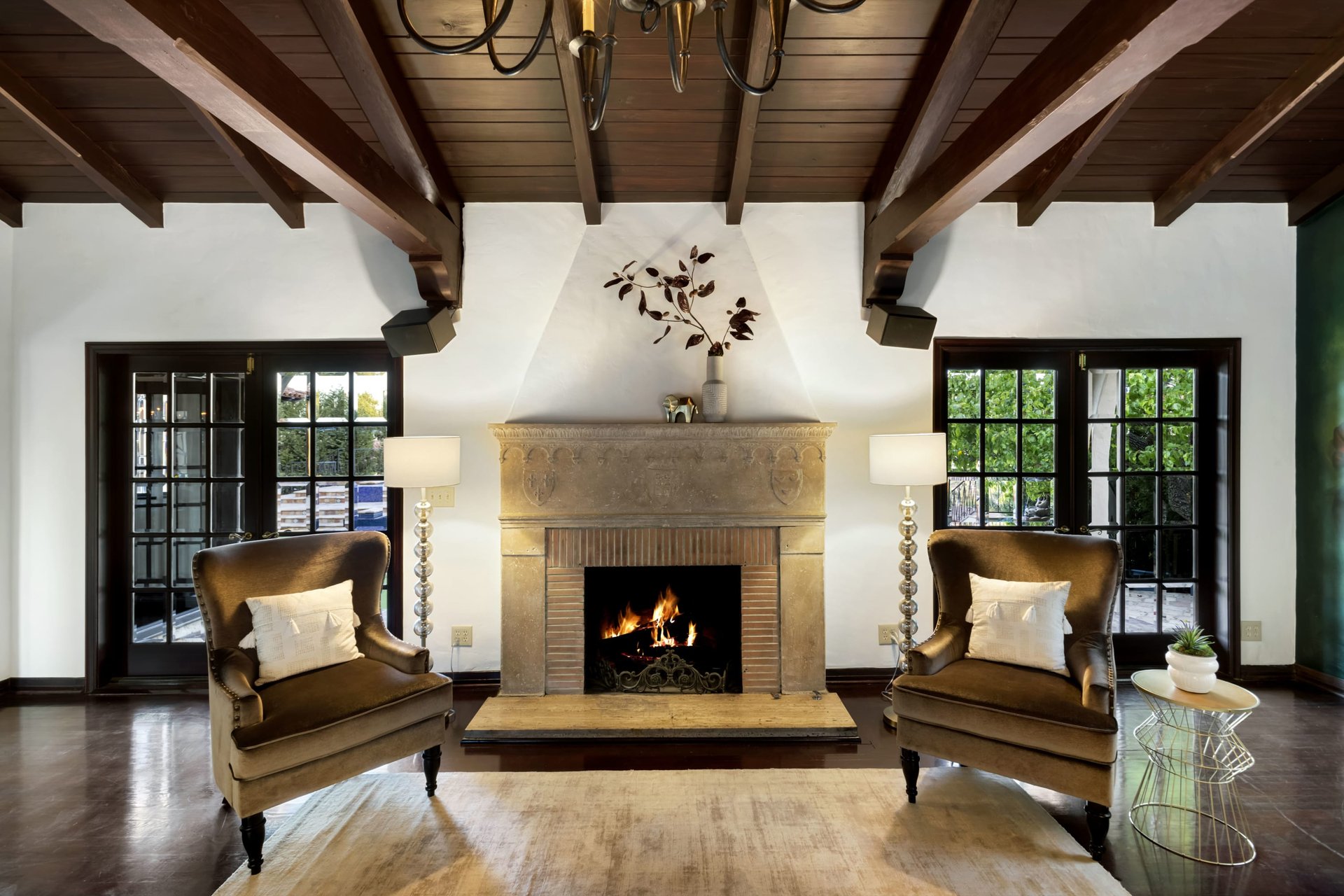 Living room with a lit stone fireplace, exposed wood beams, and matching brown armchairs.