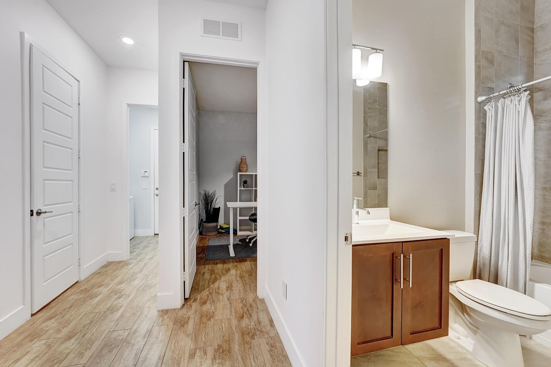 Hallway with wood-look flooring, an open office nook, and an adjoining bathroom with a wood vanity.