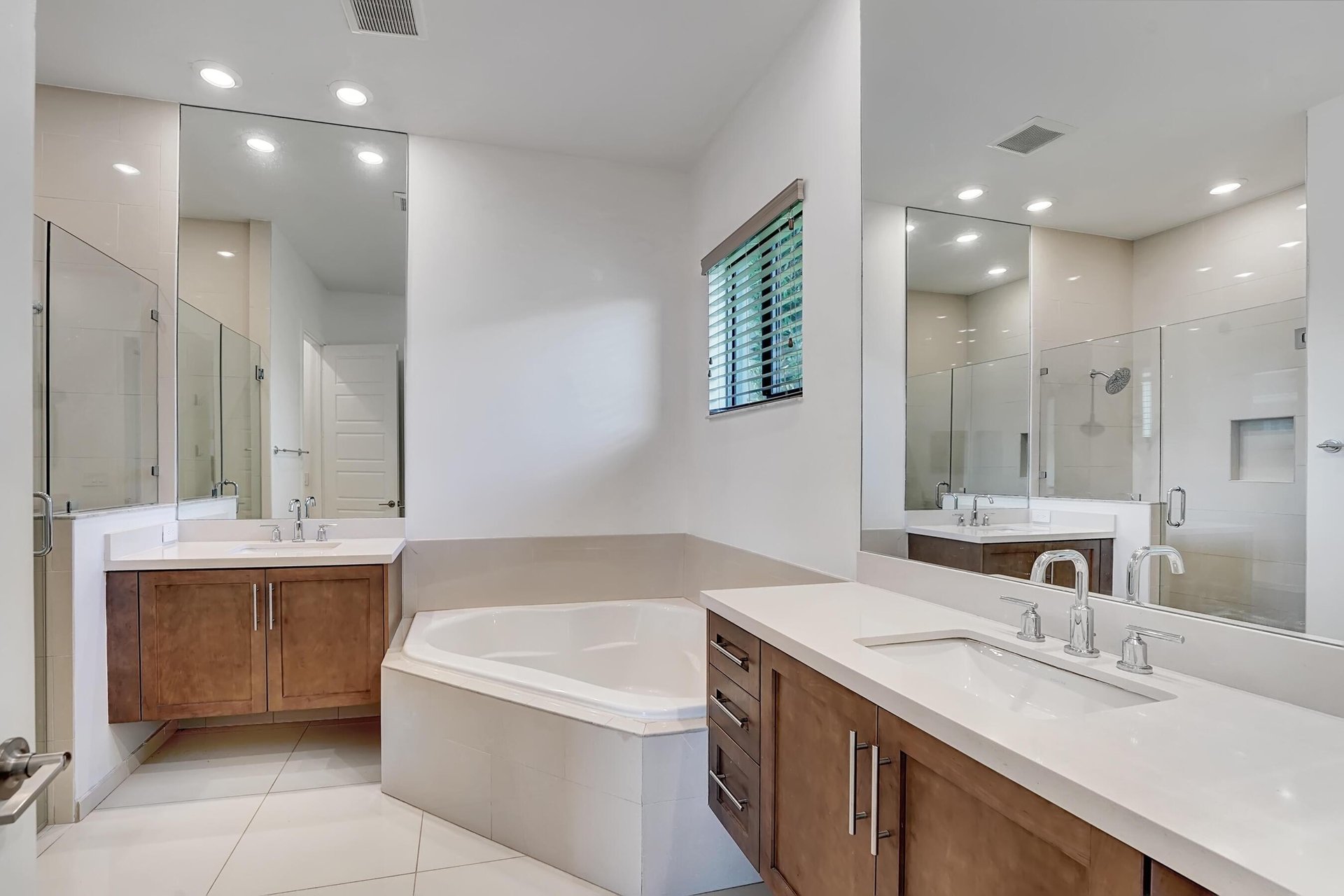 Bathroom with dual wood vanities, a corner soaking tub, and a glass-enclosed shower.
