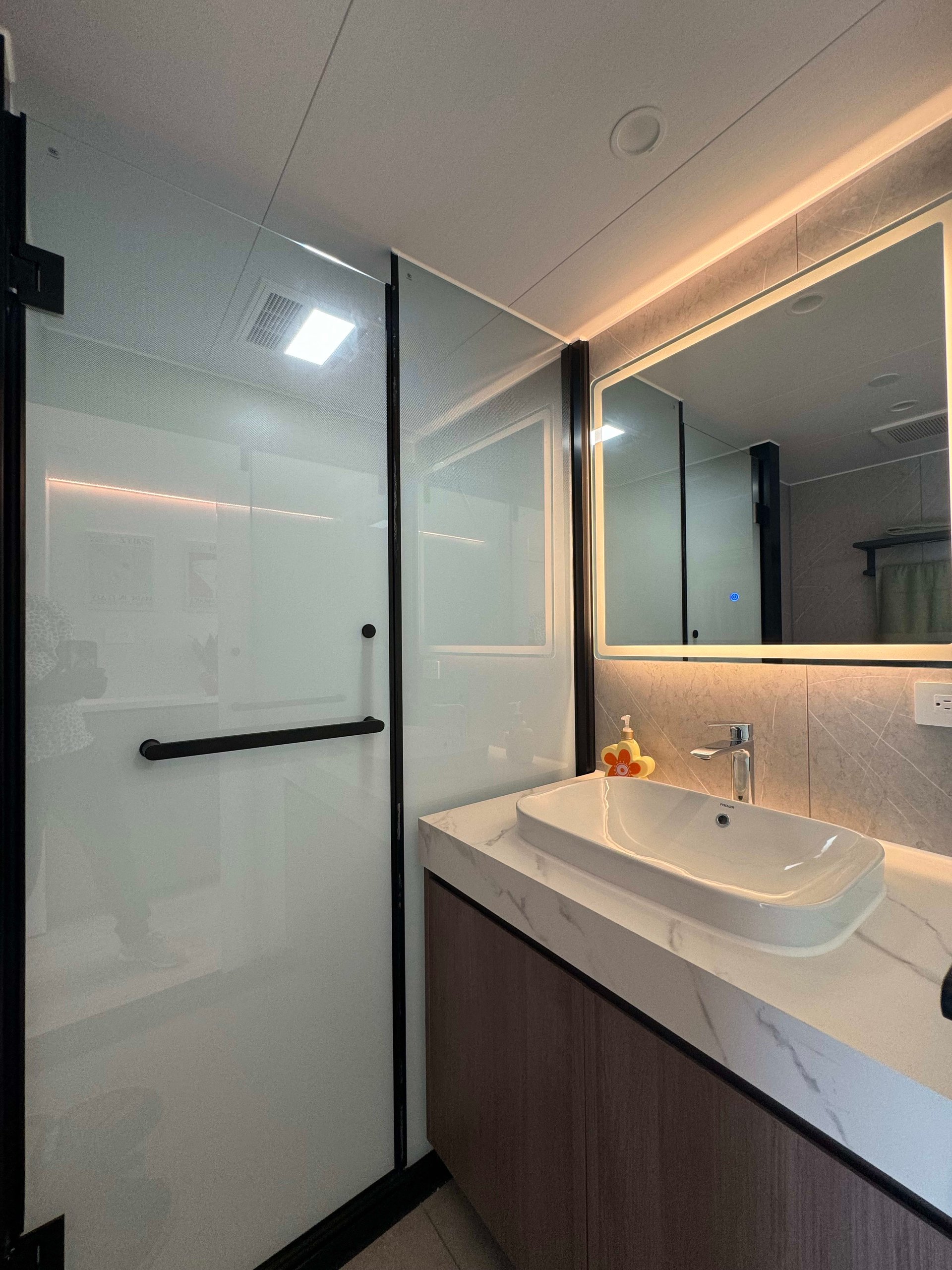 Bathroom with a frosted-glass shower, vessel sink, wood vanity, and illuminated mirror.