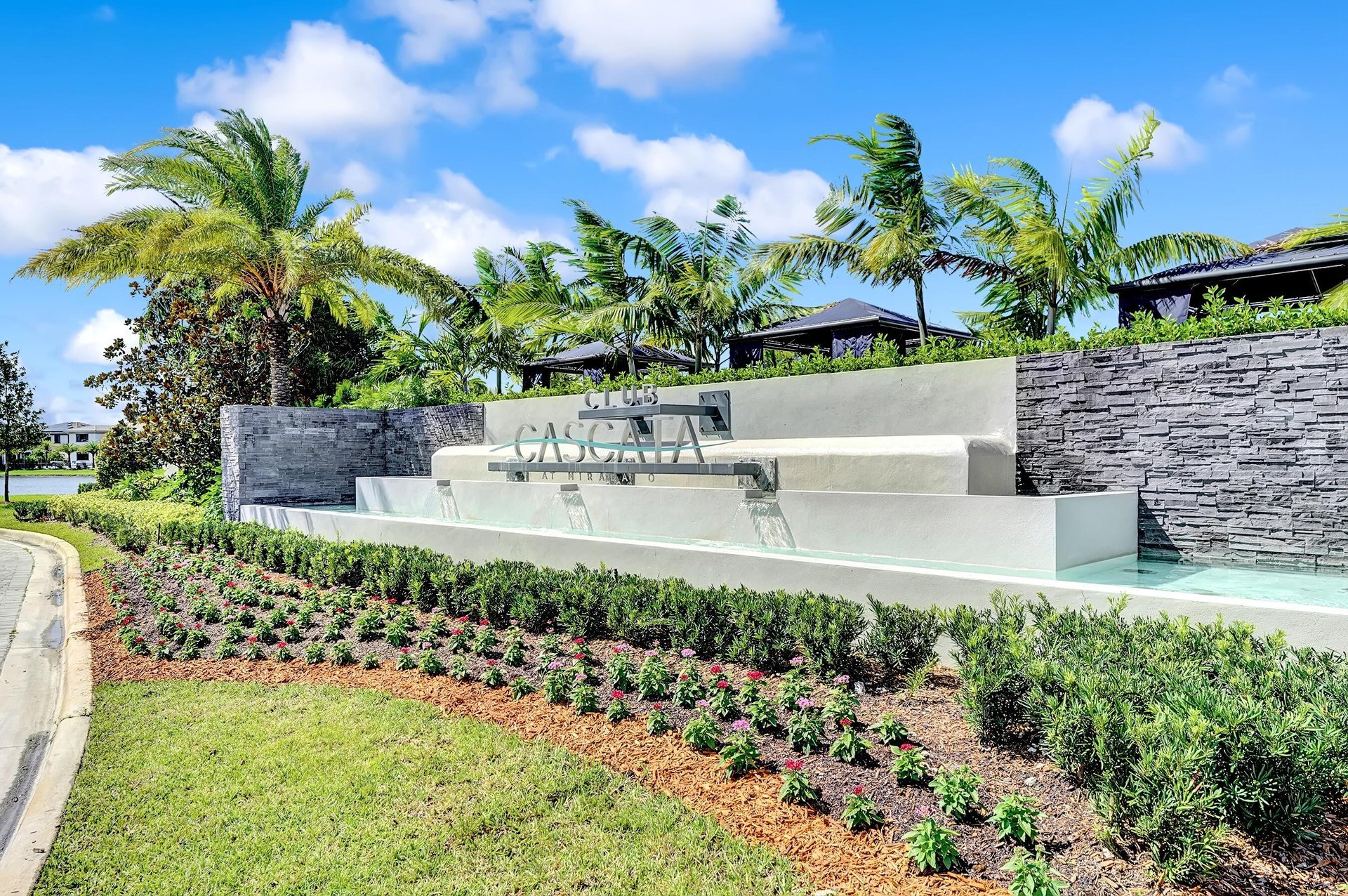 Cascata at Mirada entrance with a tiered fountain, stone walls, palms, and flower beds.