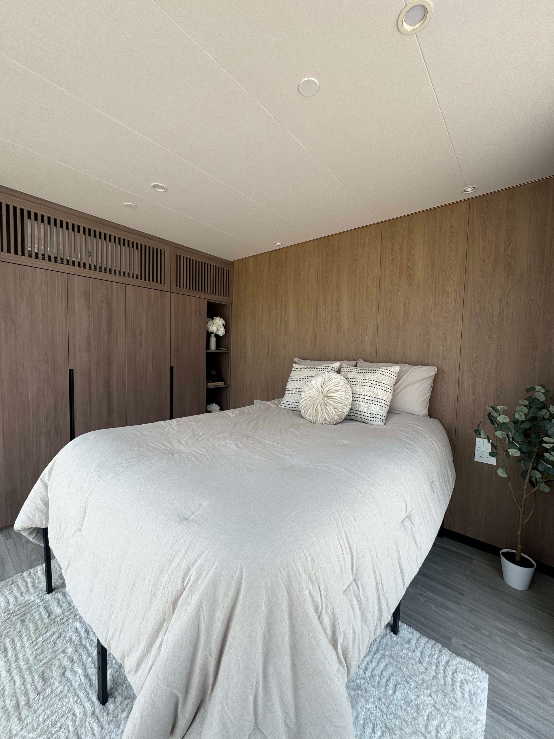 Furnished bedroom with a white bed, dark wood built-ins, and wood-paneled walls.
