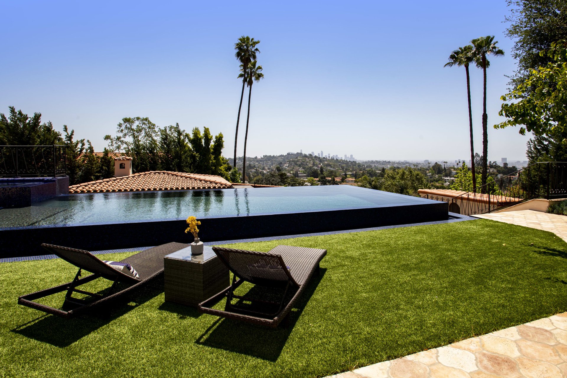 Infinity-edge pool and lawn with lounge chairs overlooking the Los Angeles skyline.