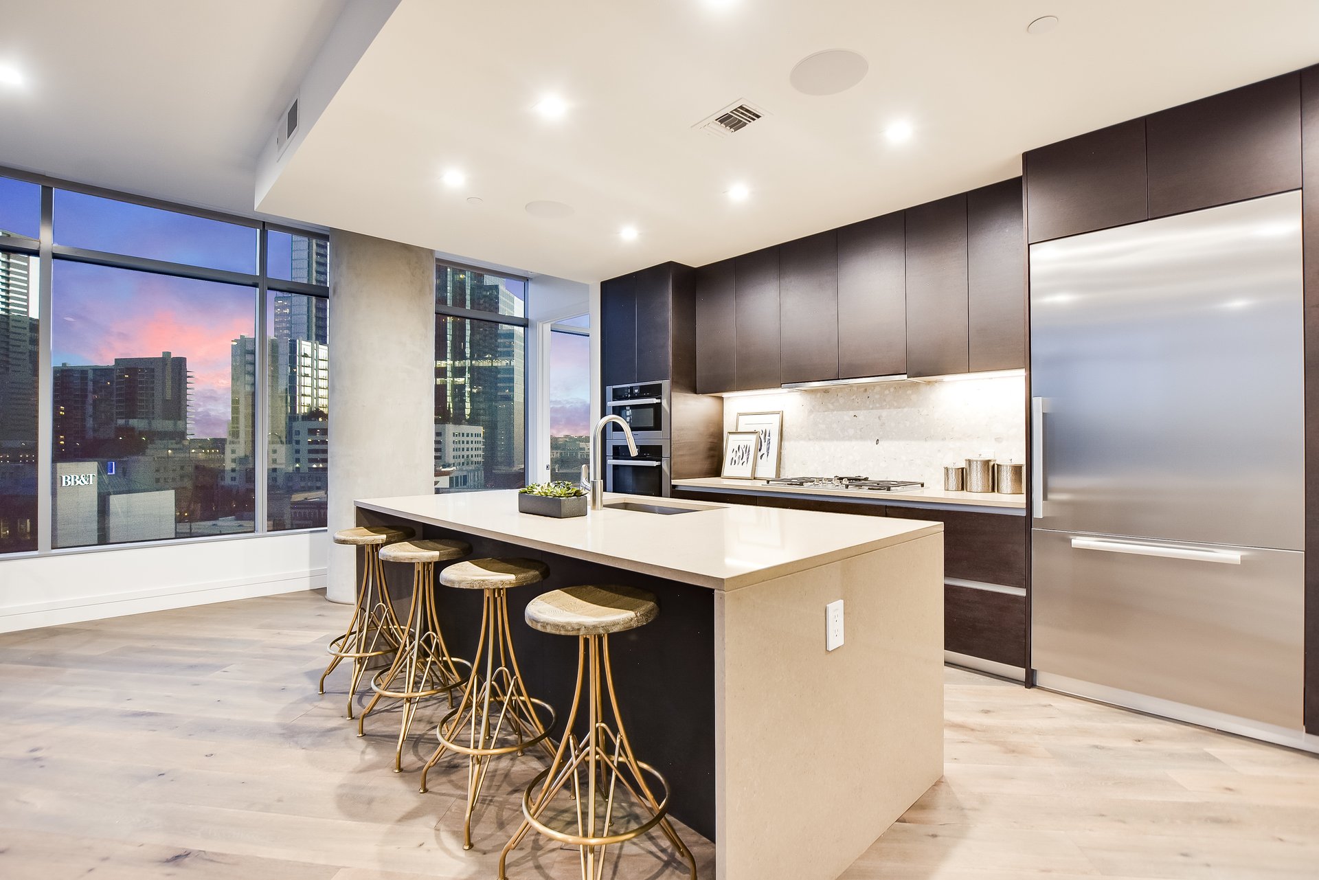 Modern condominium kitchen with a waterfall island, dark cabinetry, and downtown views through floor-to-ceiling windows.
