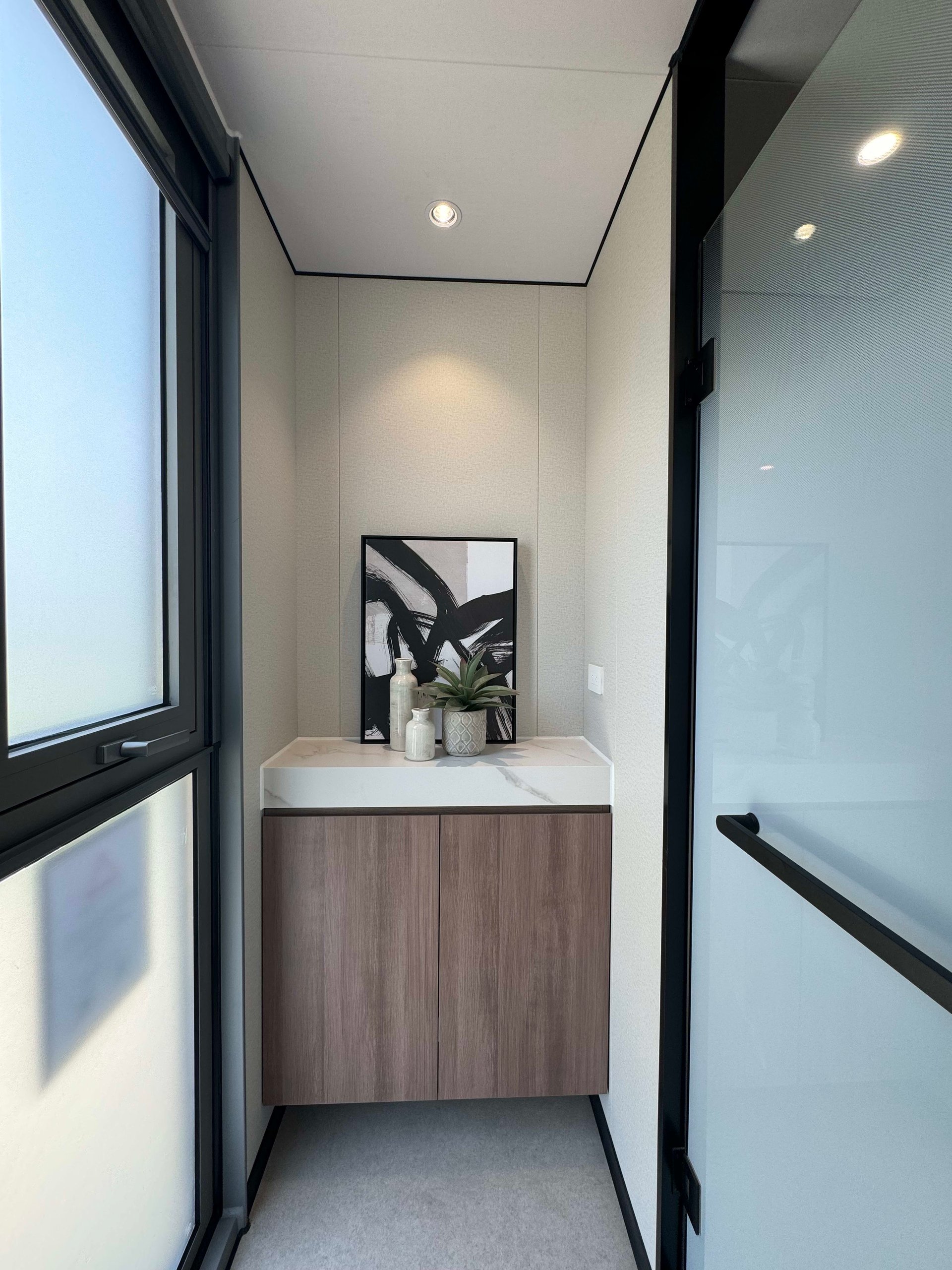 Tiny home interior nook with a wood cabinet, veined countertop, framed art, and black-framed glass doors.