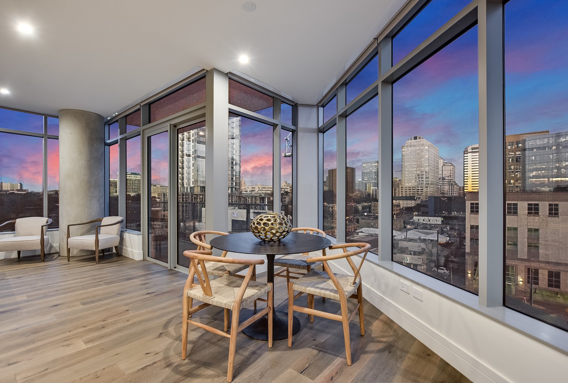 Dining area with a round table and floor-to-ceiling windows overlooking the Austin skyline at dusk.
