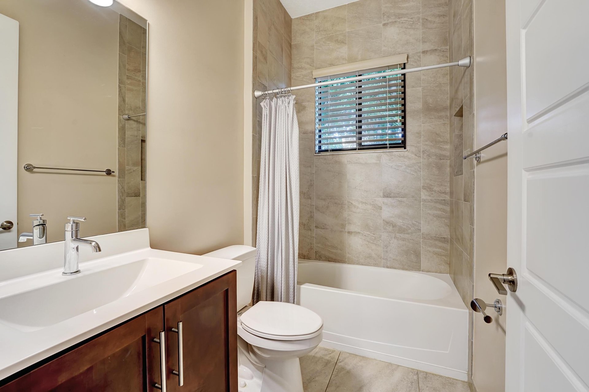 Bathroom with a tiled tub and shower, white curtain, and dark wood vanity.