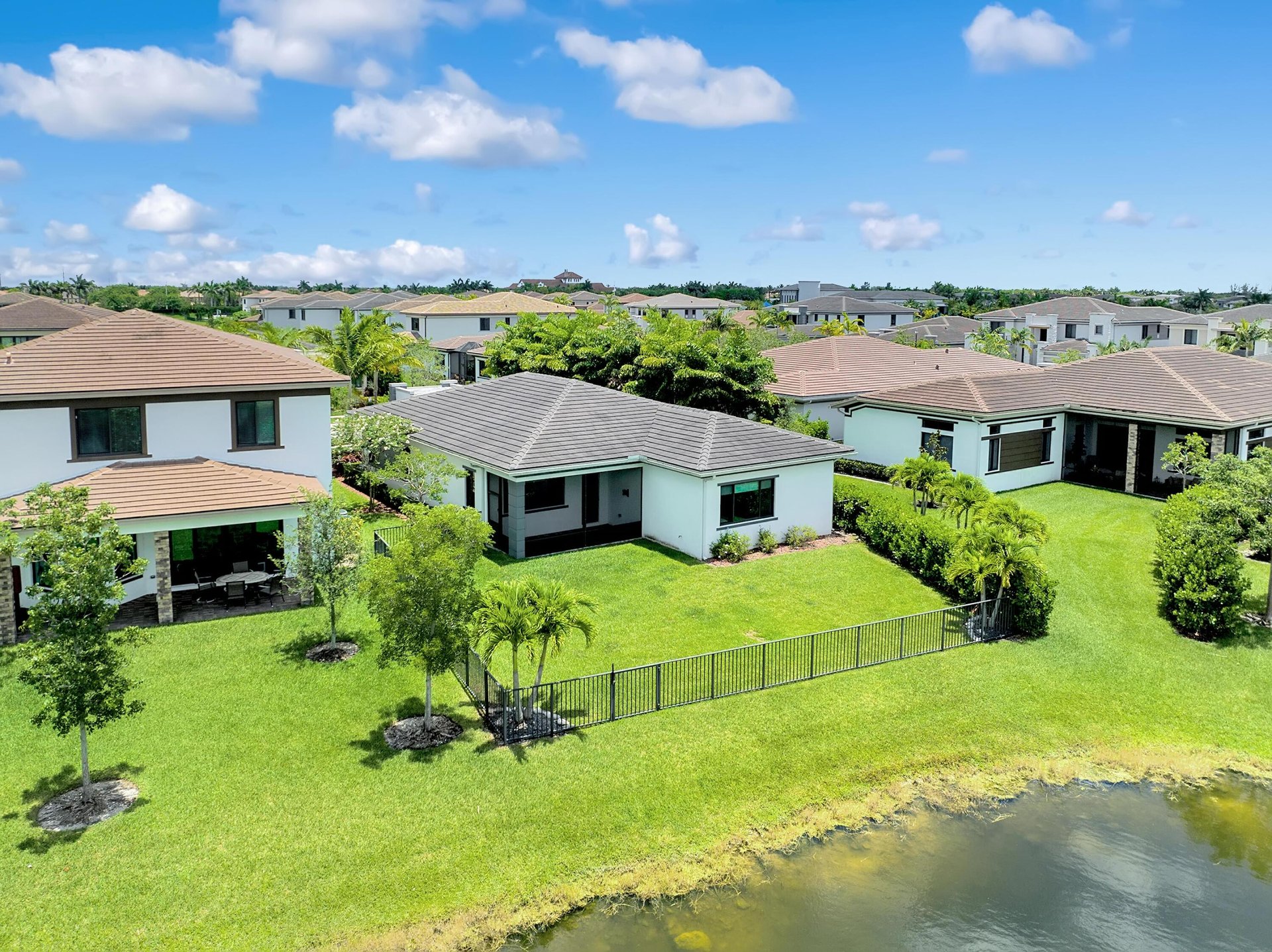 Aerial view of a home with a fenced lawn beside a canal, surrounded by neighboring houses.