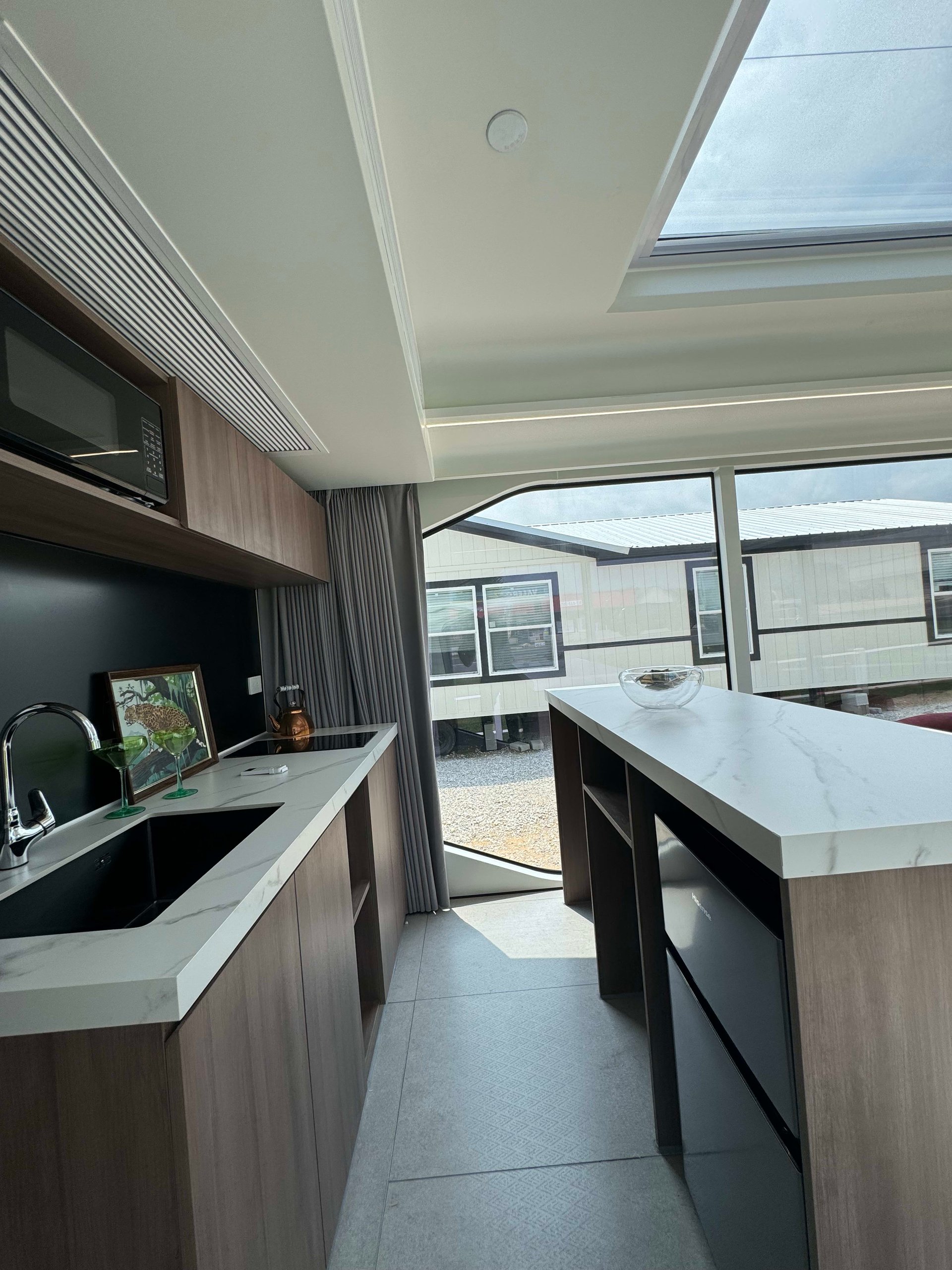 Tiny-home kitchen with a marble-look island, wood cabinetry, and skylight.