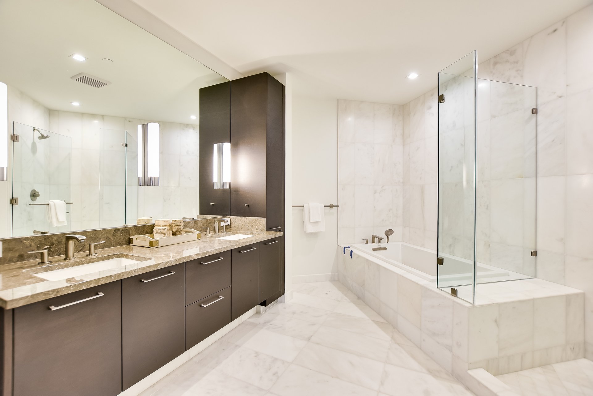 Marble bathroom with a dark double vanity and a soaking tub behind a glass shower screen.