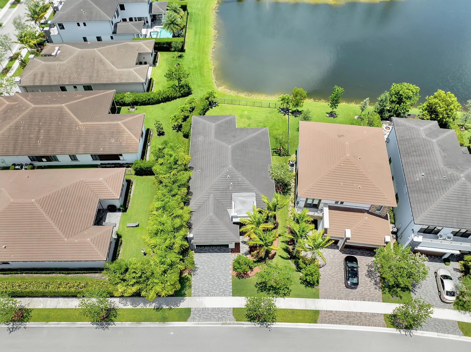Aerial view of a gray-roofed home with palms beside a neighborhood lake.