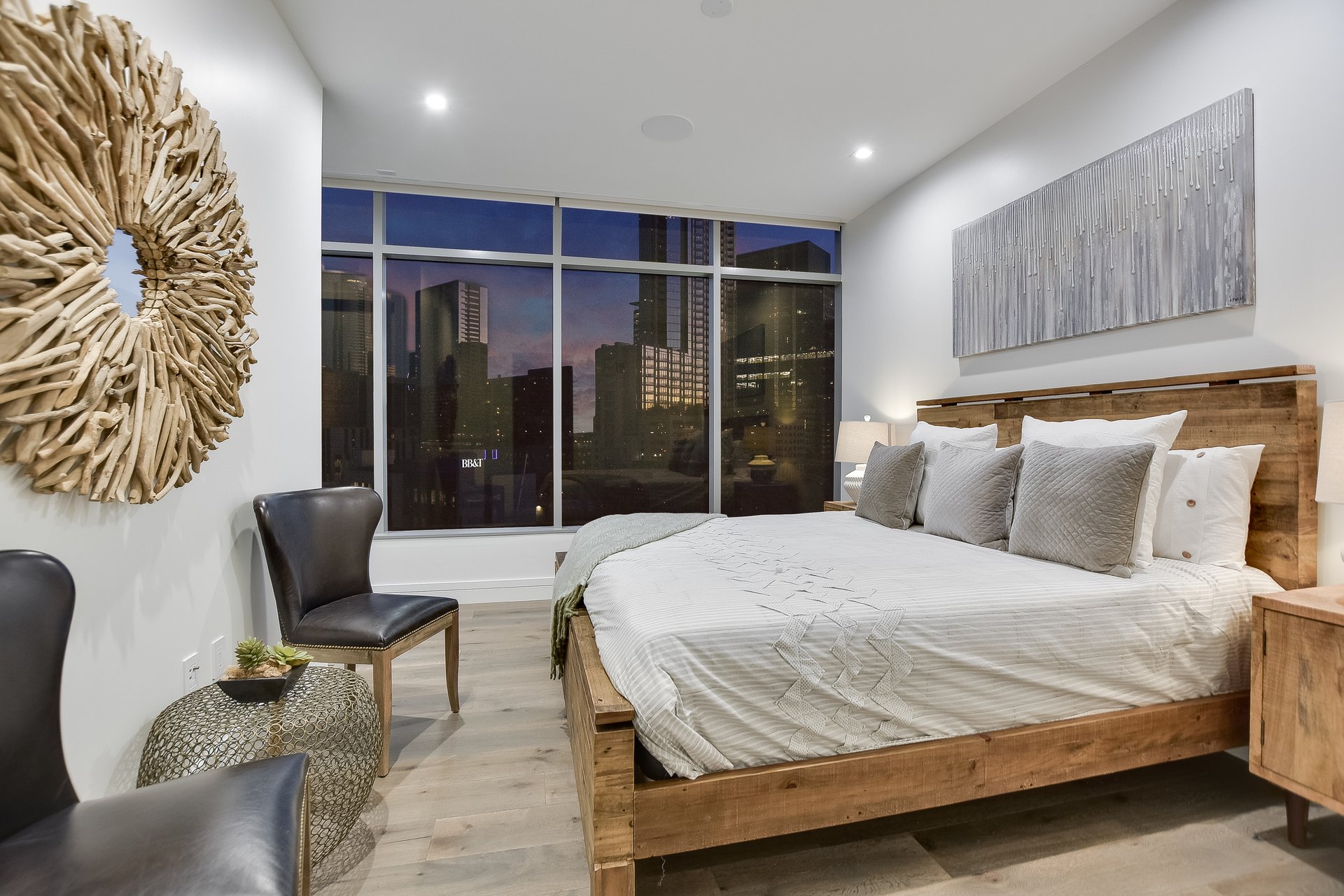 Modern bedroom with a wood platform bed and city skyline views through floor-to-ceiling windows.