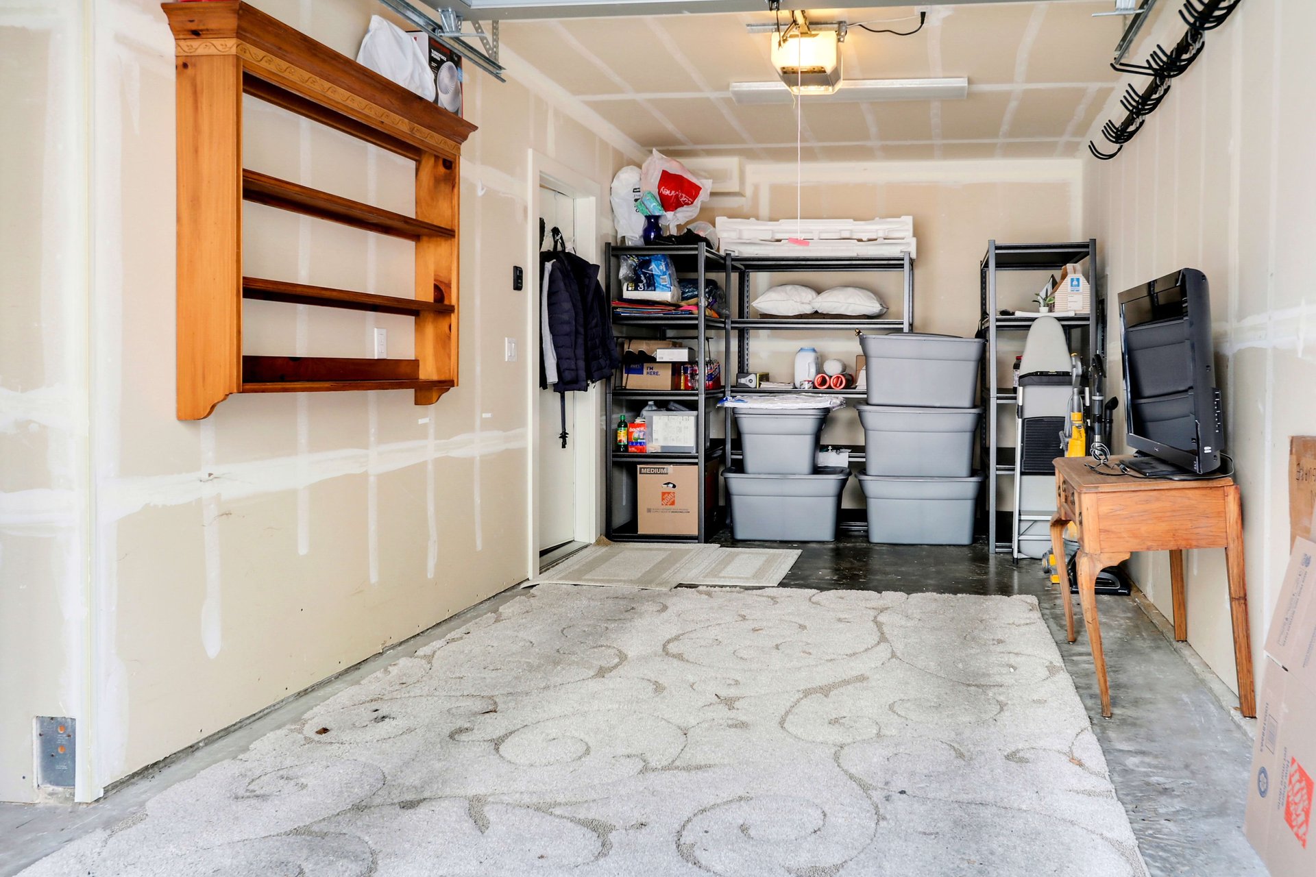 Garage interior with storage shelves, plastic bins, a wall-mounted wooden shelf, and a workbench.