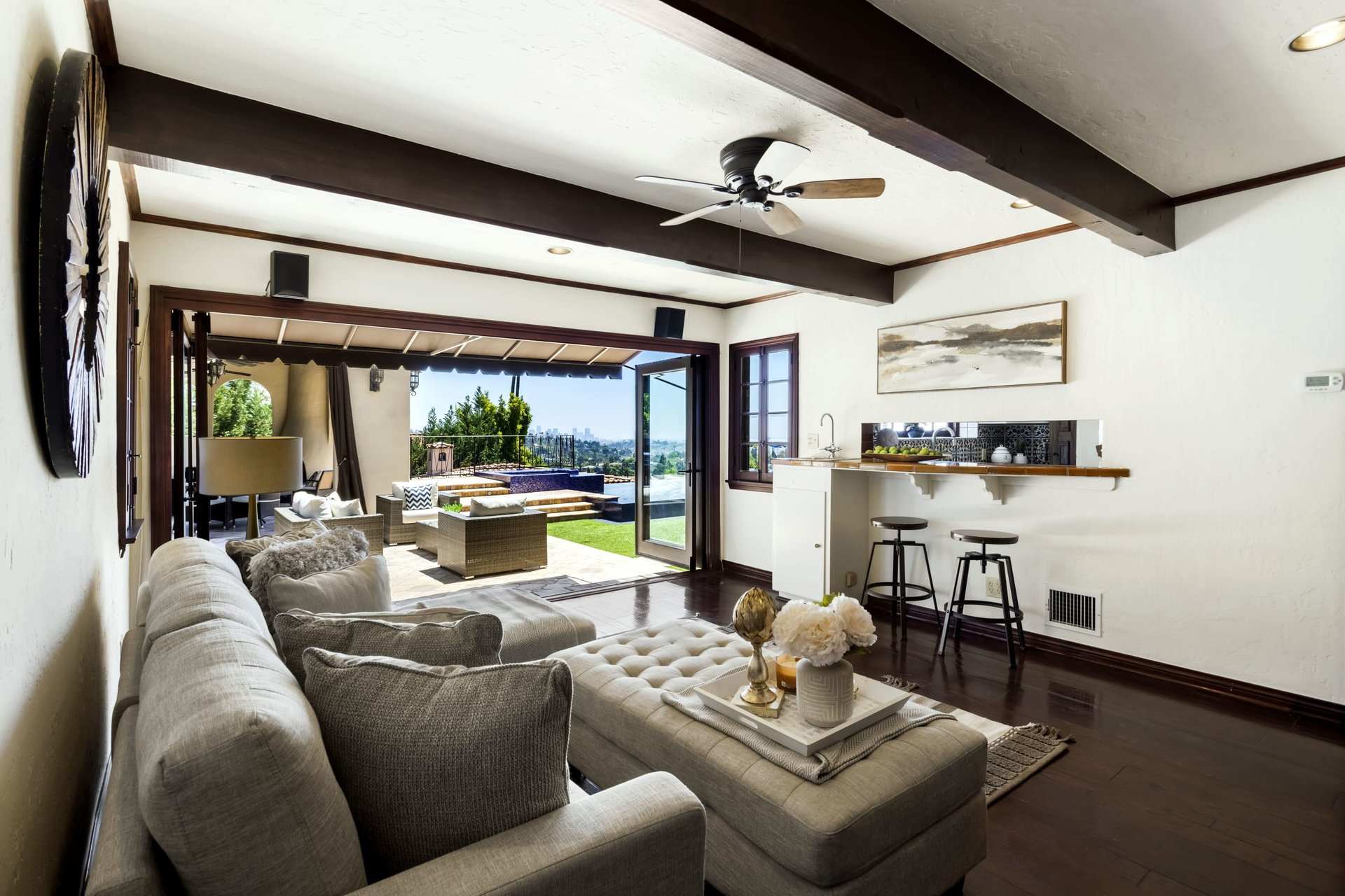 Living room with dark ceiling beams, sectional seating, and wide doors opening to a patio and city view.