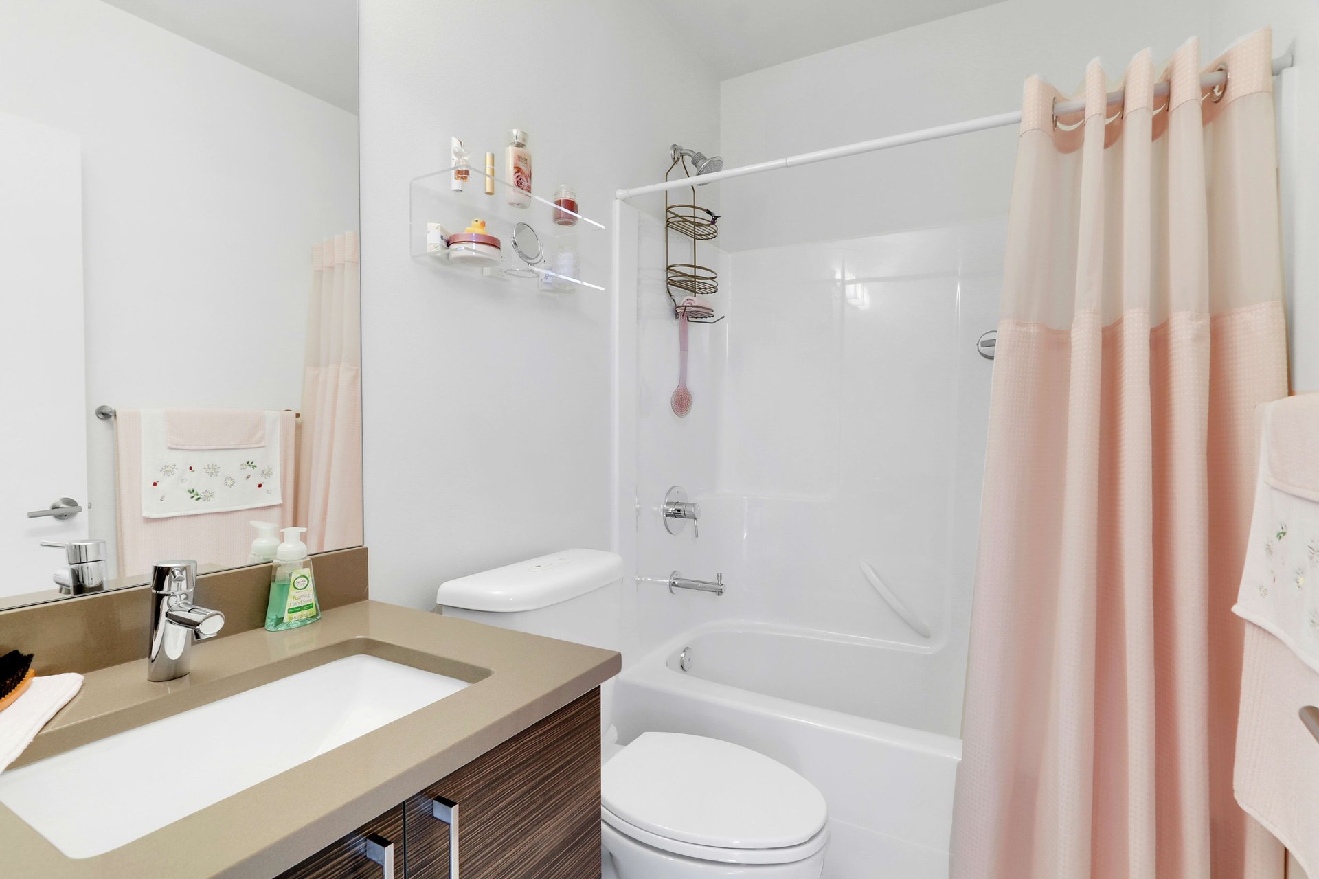 Bathroom with a brown vanity and white tub-shower behind a pale pink curtain.