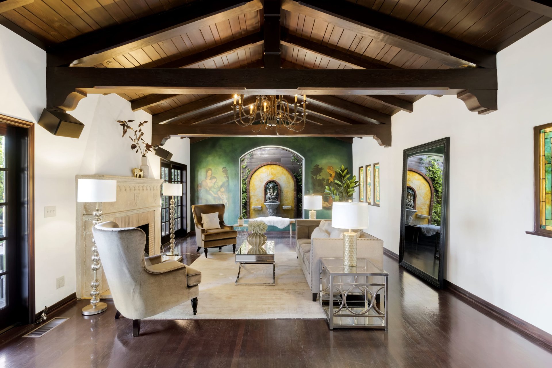 Living room with exposed wood beams, a stone fireplace, and a green fountain wall.
