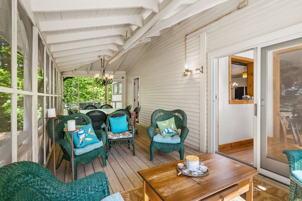 Screened porch with wicker chairs, colorful cushions, and white exposed-beam ceiling.