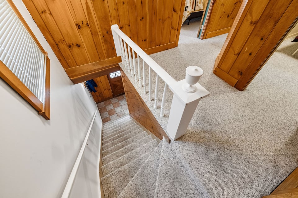 Carpeted staircase with white railings and honey-toned wood-paneled walls.
