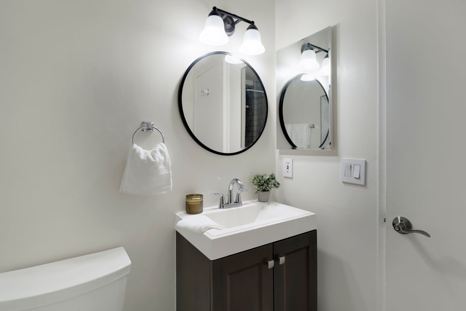 Bathroom vanity with a white sink, dark wood cabinet, round mirror, and chrome fixtures.