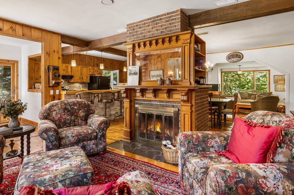 Living room with an ornate wood-and-brick fireplace, exposed beams, and floral seating.