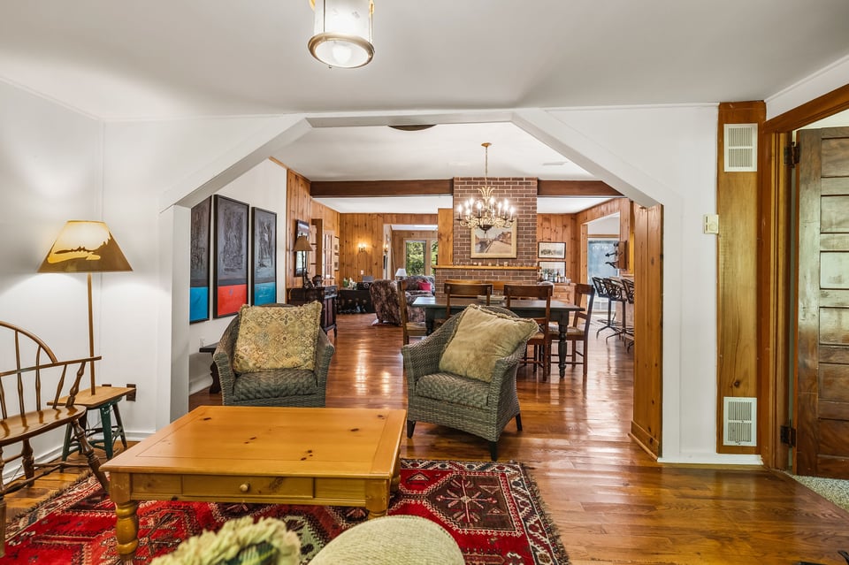 Living and dining area with wood-paneled walls, brick fireplace, and hardwood floors.
