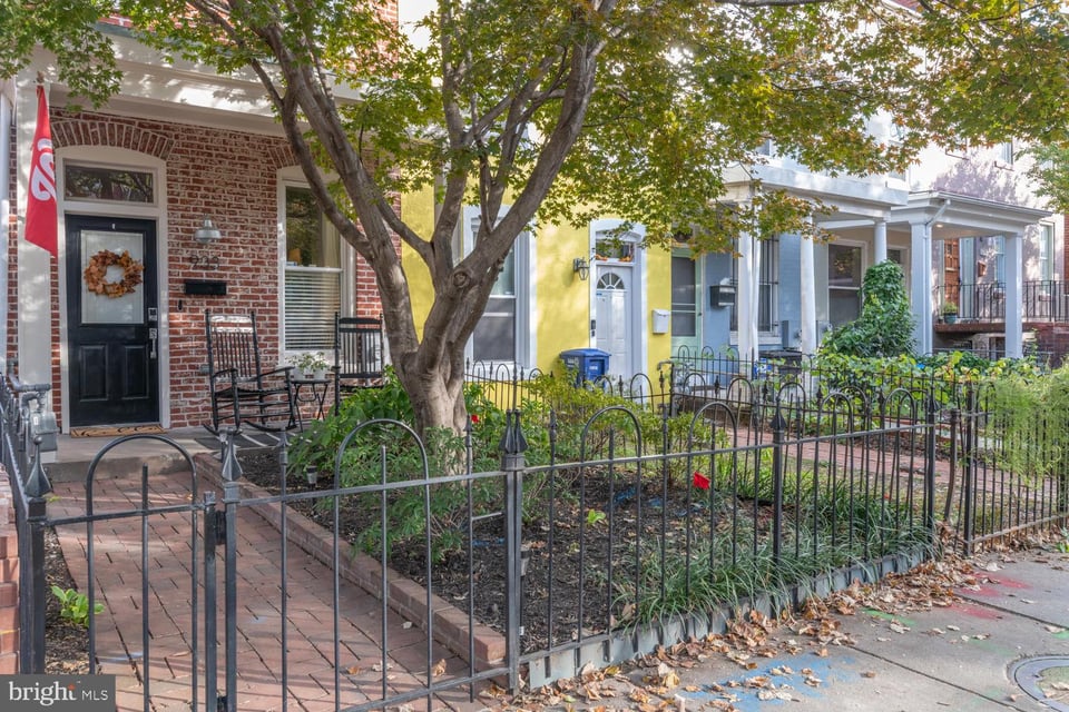 Attached row houses with fenced front gardens, brick walkways, and a large shade tree.