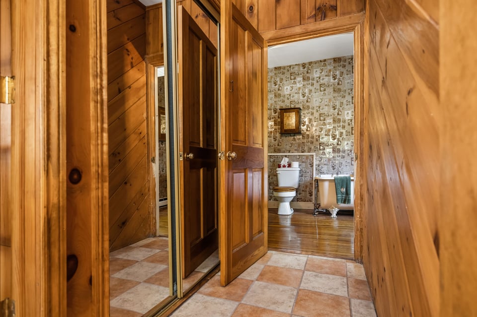 Bathroom beyond a wood-paneled hallway, with vintage patterned wallpaper and a clawfoot tub.
