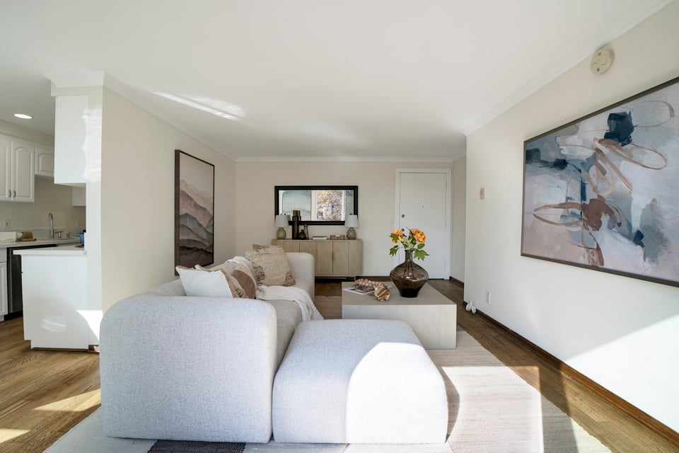 Living room with a white sectional sofa, abstract wall art, and flowers on the coffee table.