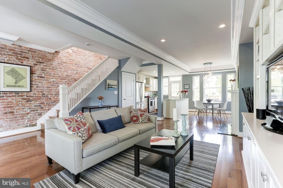 Living room with exposed brick wall, white staircase, and open kitchen and dining area.