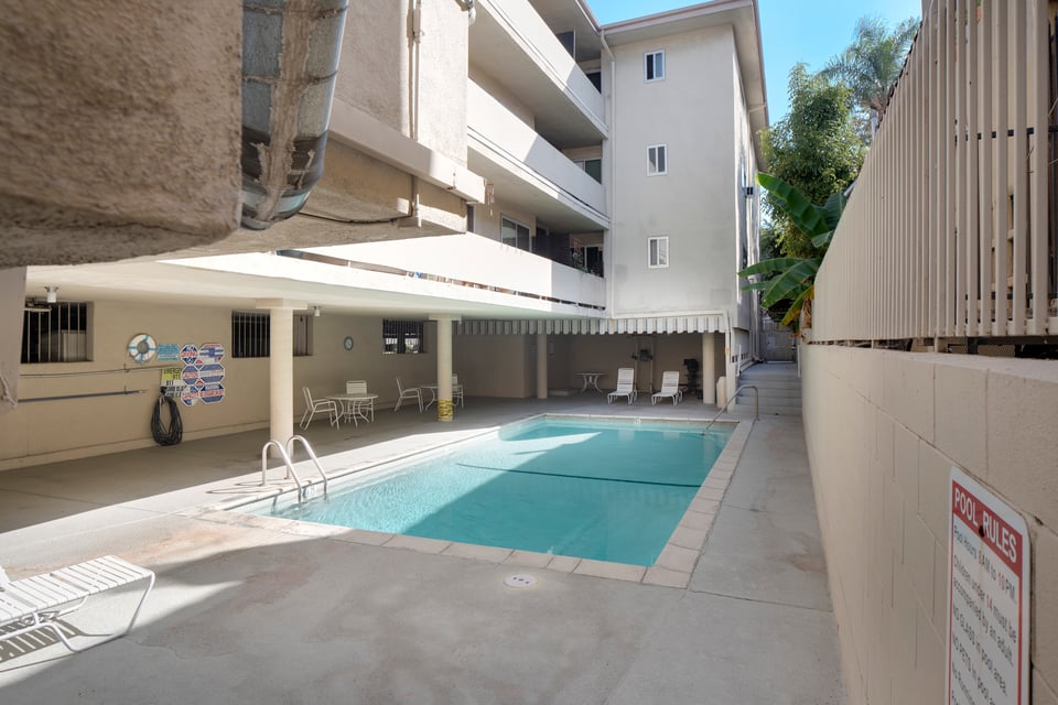 Apartment courtyard pool with patio chairs and a Pool Rules sign.
