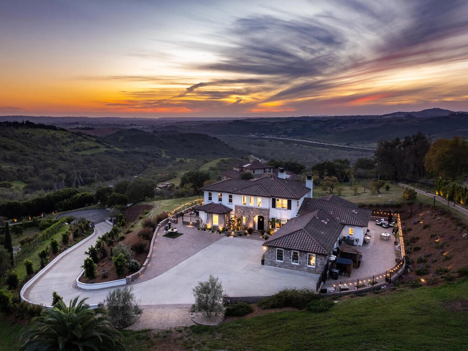 Aerial view of a hillside estate with a curved driveway beneath a vivid sunset sky.