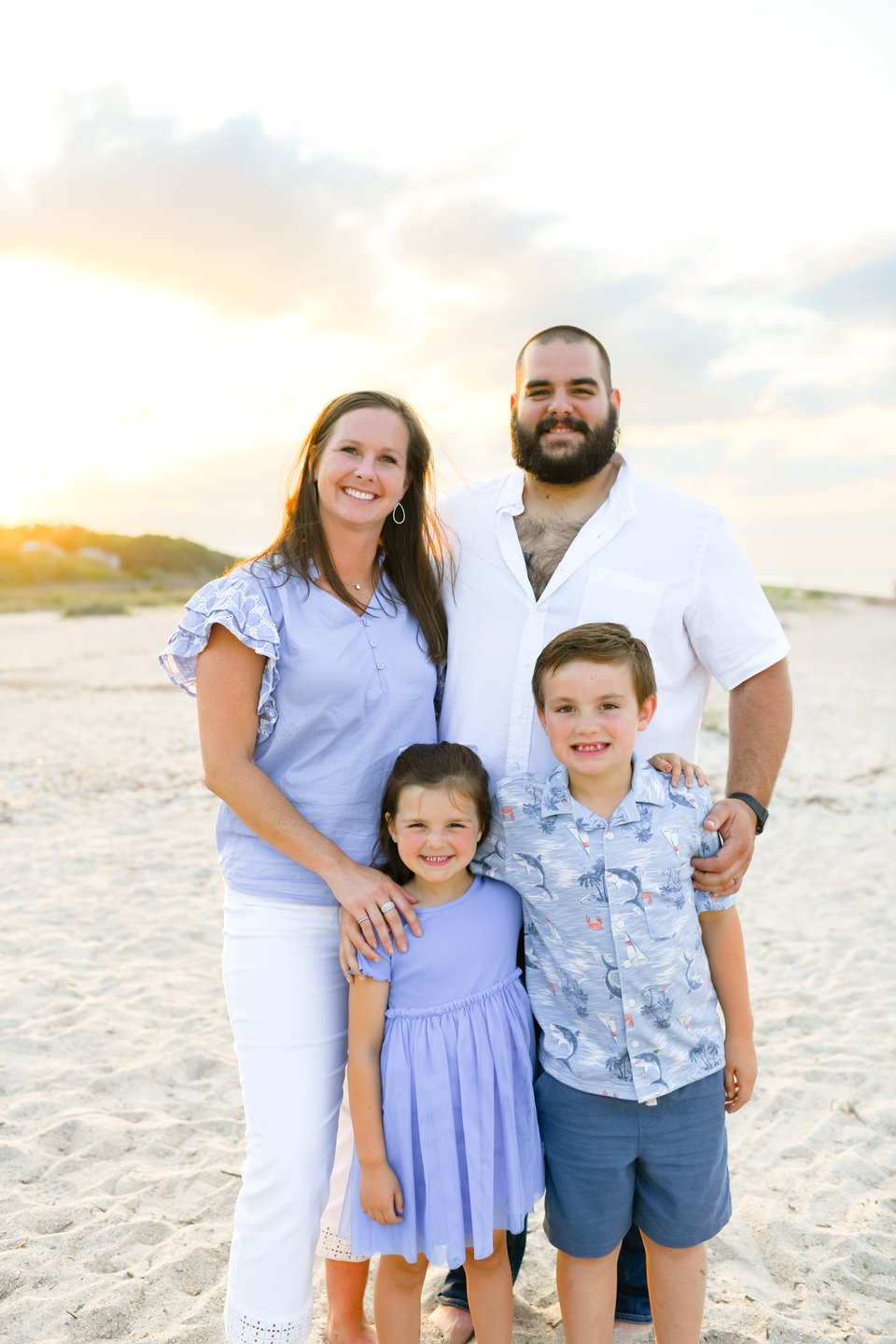Family of four posing on a beach at golden hour, with two adults and two children.