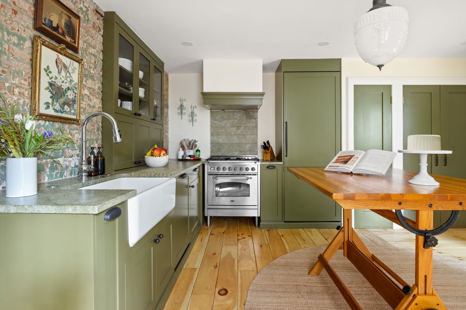 Kitchen with sage-green cabinets, exposed brick, a farmhouse sink, and a large wooden table.