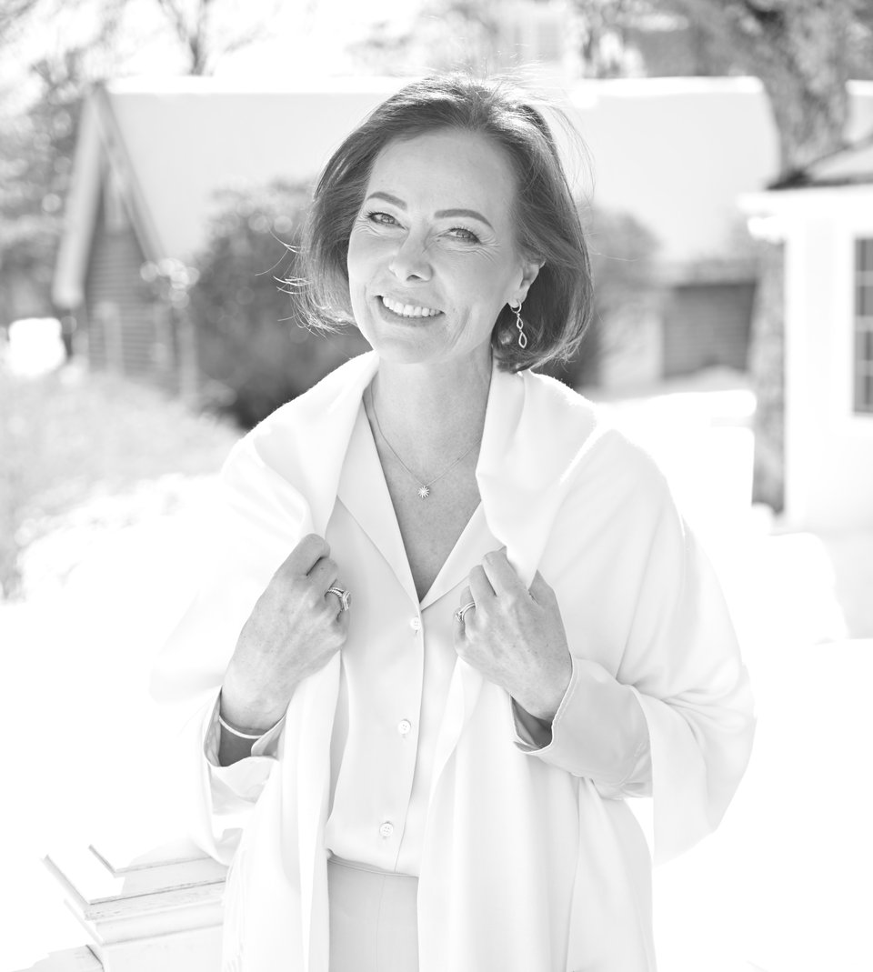 Smiling woman in a white outfit seated outdoors.