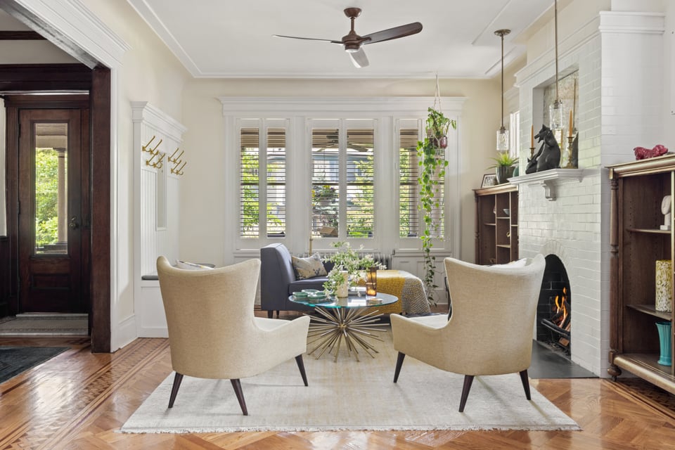 Living room with a white brick fireplace, shuttered windows, and parquet floors.