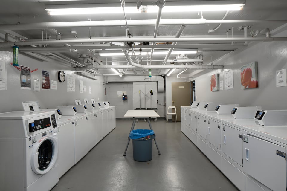 Shared laundry room with rows of white washers and dryers and a central folding table.