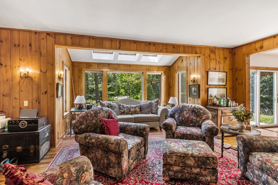 Wood-paneled living room with floral seating, skylights, and windows overlooking trees.