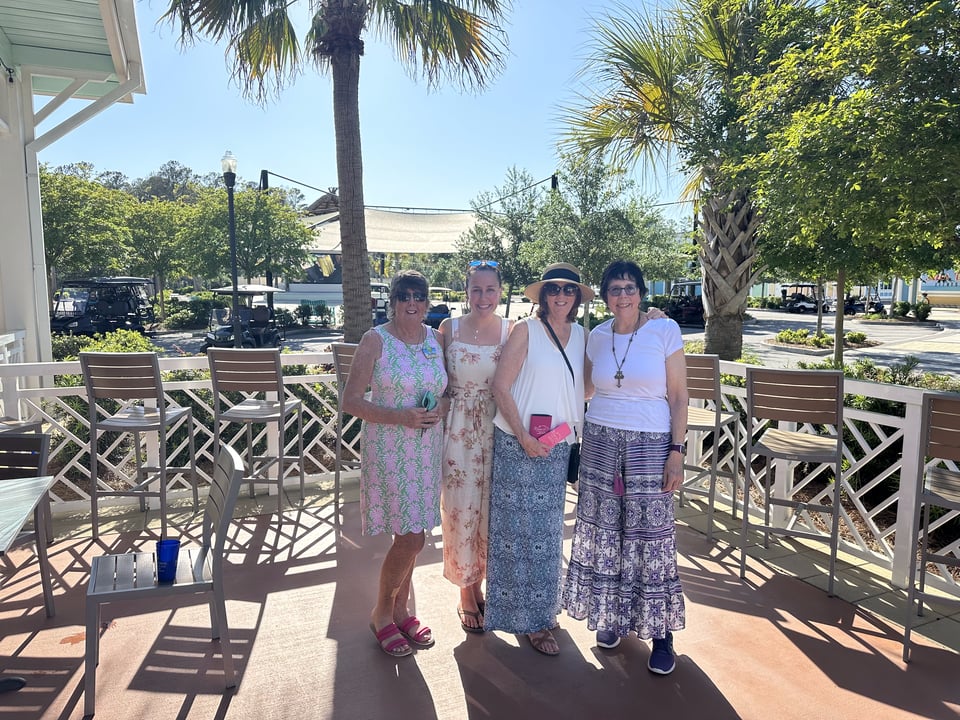 Four women pose together on a sunny outdoor patio.