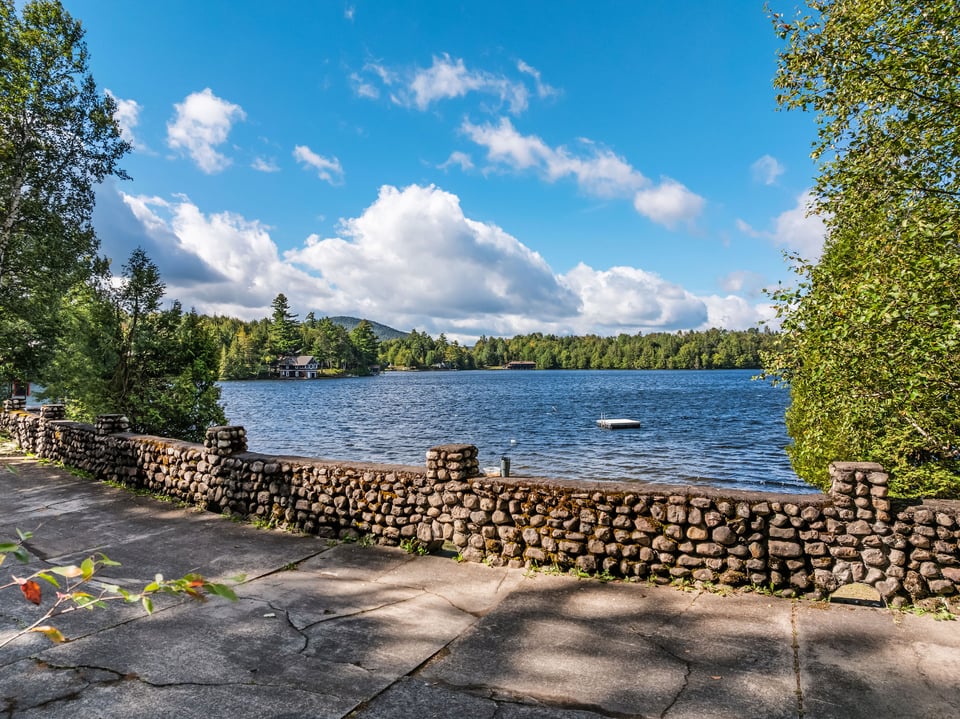 Lake view with a stone wall in the foreground and a floating dock on the water.