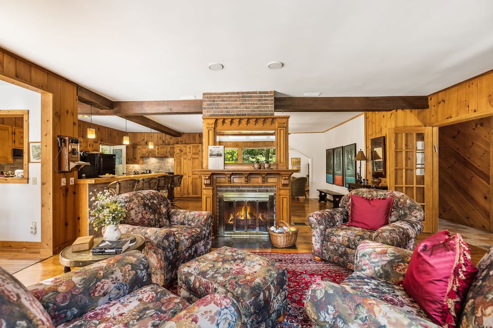 Living room with ornate wooden fireplace, floral seating, and wood-paneled walls.