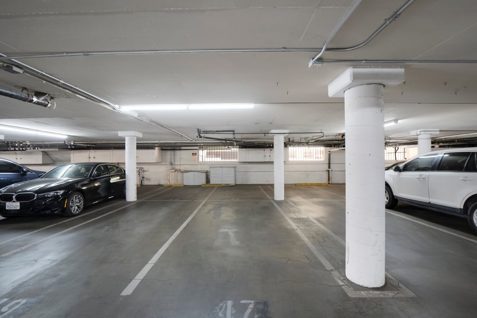 Underground parking garage with marked spaces, white columns, and cars parked along the sides.