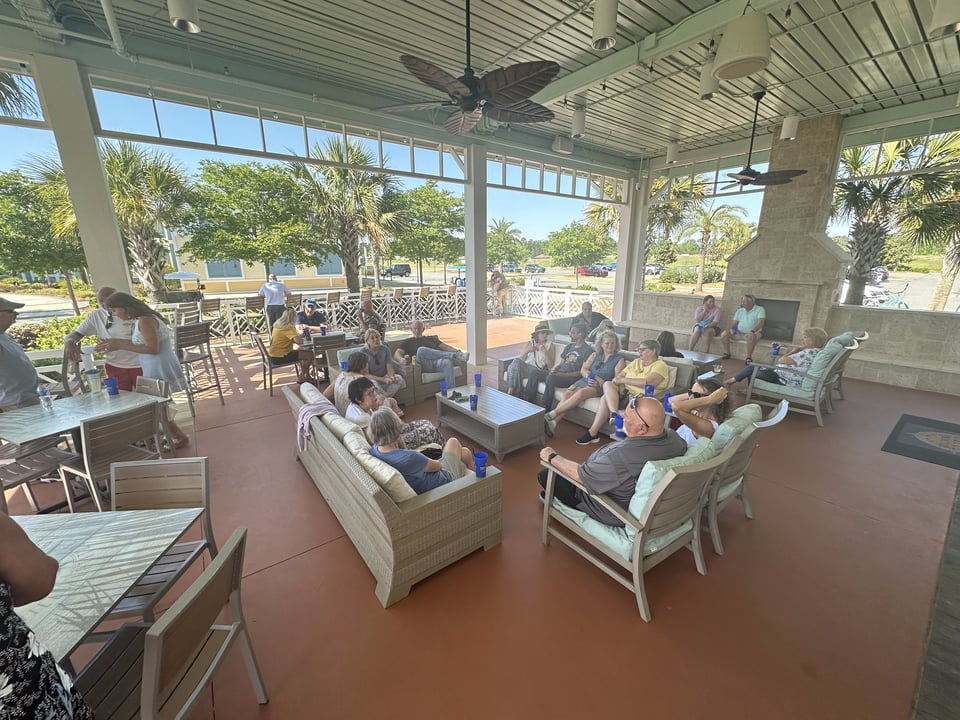 People socialize on a covered patio with lounge seating and a stone fireplace.