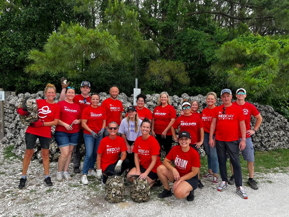 Real estate agents in red REDDAY shirts pose beside a stone wall and piles of rocks.