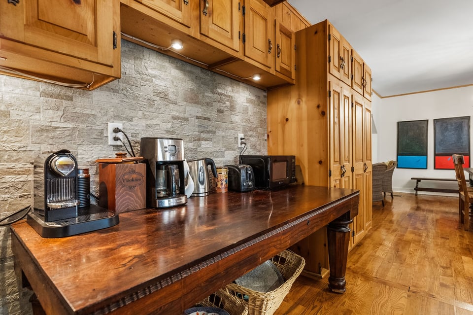 Kitchen with wood cabinetry, stone backsplash, and a long counter lined with coffee appliances.