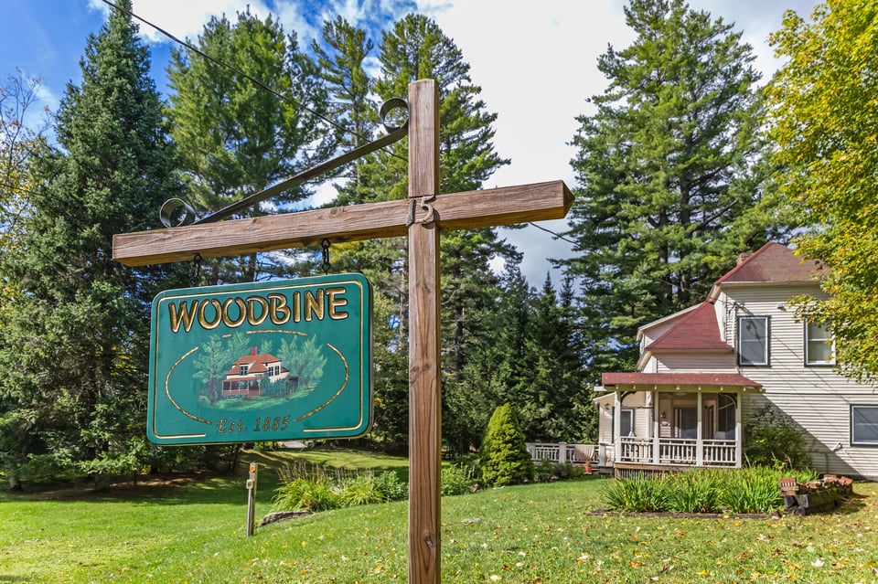 Camp Woodbine entrance sign beside a white house with a covered porch.
